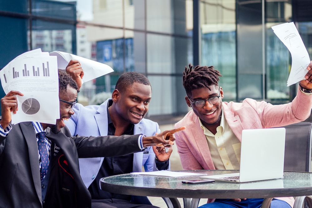 a group of their three successful African American businessmen in a stylish suit sit at the table and work with a laptop online conference and throw papers up . teamwork and success concept