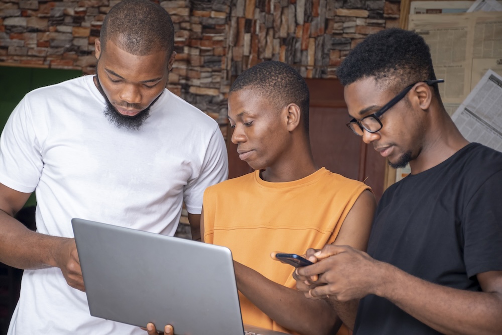 Group of young African males discussing a project while using their laptop and phones