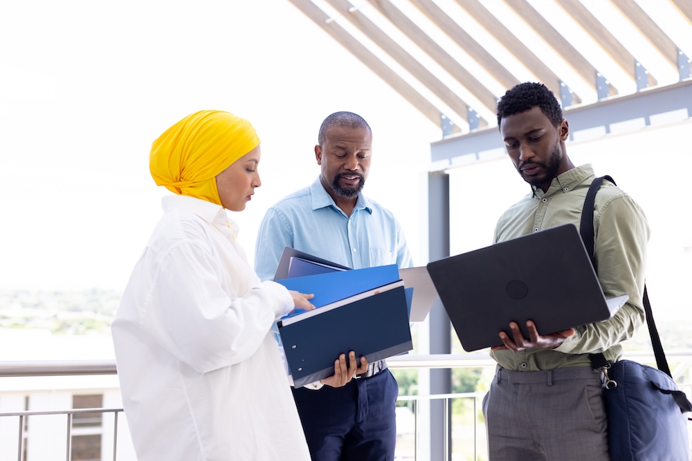 Happy diverse business people discussing and holding documents outside office. Global business, finances and office concept.