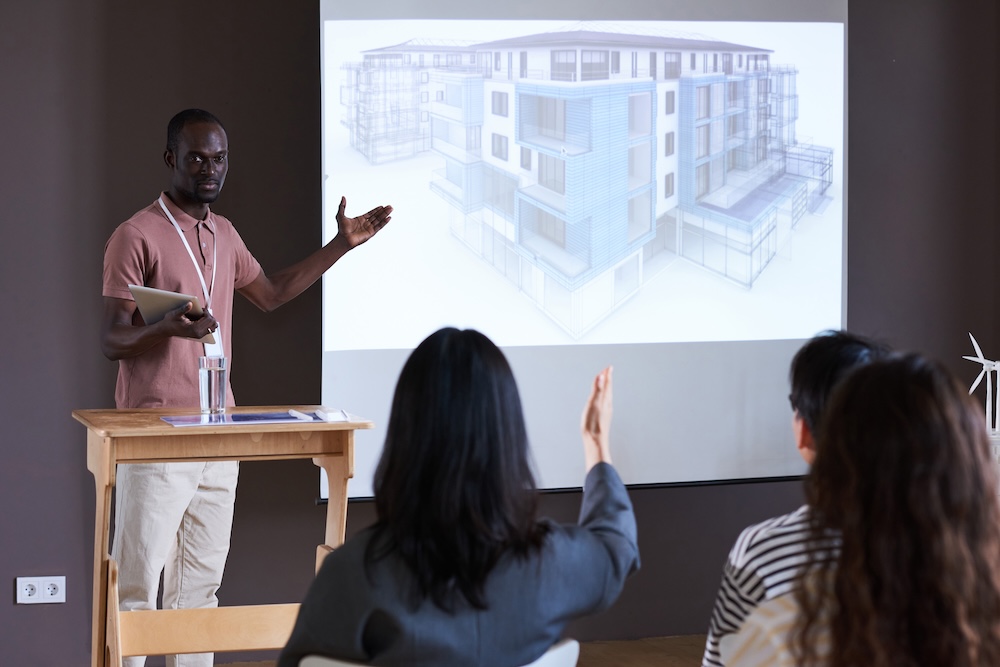 African young architect with digital tablet pointing at whiteboard with new modern building during a presentation