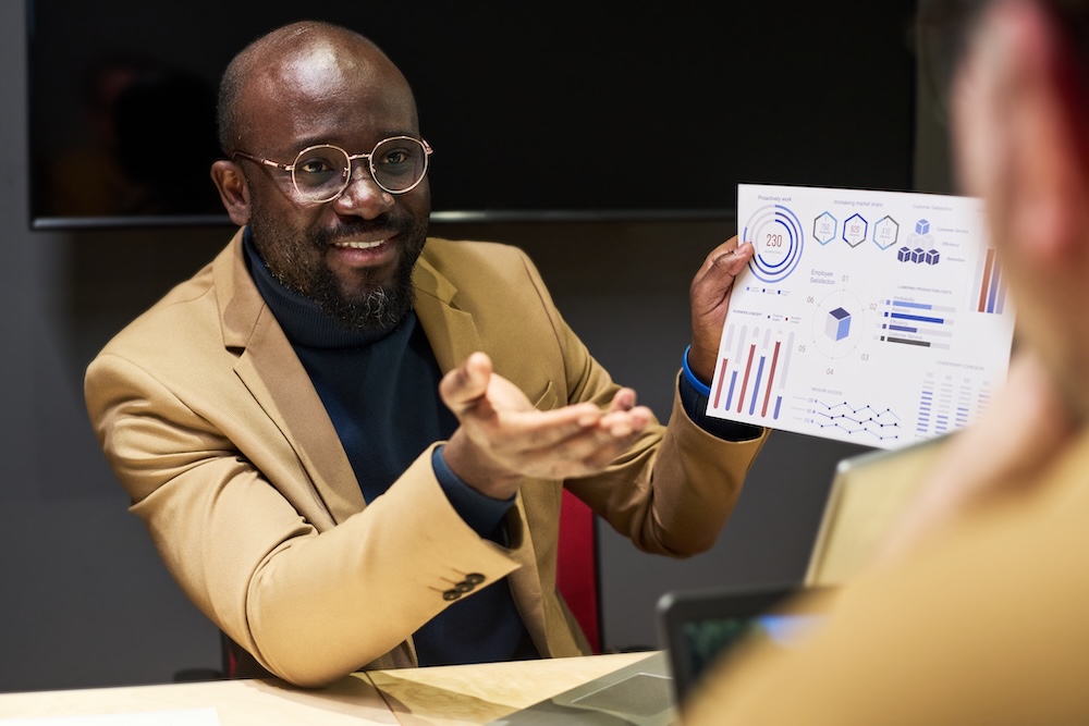 Young confident analyst with financial paper document talking to colleague