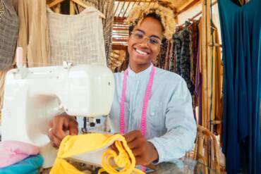 african american woman sewing a stylish yellow swimming suit for summer pool party in tropical workshop in Bali