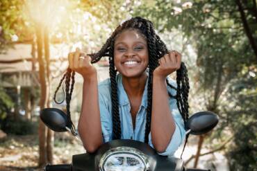 Charming young african american girl woman with a perfect smile and black pigtails sitting on a motobike,